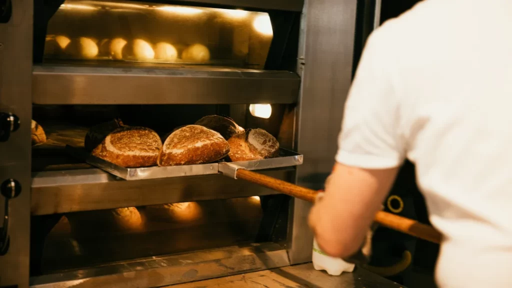 Professional Oven for Your Bakery: Which One to Buy? 1 A person removes freshly baked bread from a professional oven, showcasing the baking process in a kitchen setting.