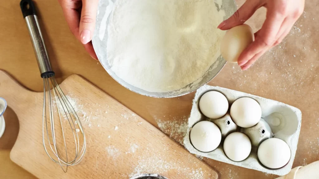 Industrial Baking Equipment: Boost Your Production Efficiency 1 A person using a whisk to mix eggs and flour in an industrial baking setting.